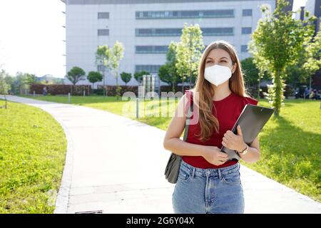 Business girl with protective mask walks holding folders in her hands with office buildings on the background Stock Photo