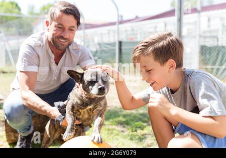 Dad and his son taking care of abandoned dog in animal shelter playing with him Stock Photo