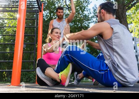 Low-angle view of an athletic couple clapping hands while doing crunches face to face during workout routine in a modern fitness park Stock Photo