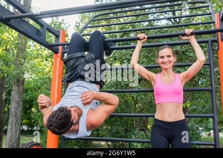 Happy fit young woman and her workout partner doing crunches and vertical leg raises for abdominal muscles outdoors in a modern calisthenics park Stock Photo