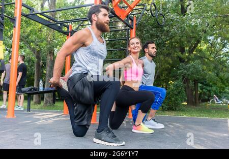 Full length side view of three determined friends doing stretching exercises for legs, as warming up or cool down routine outdoors in a modern fitness Stock Photo