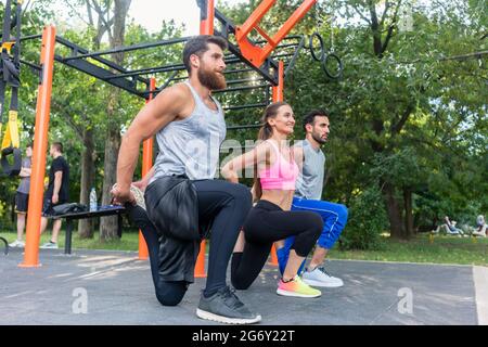 Full length side view of three determined friends doing stretching exercises for legs as warming up, or cool down routine outdoors in a modern fitness Stock Photo