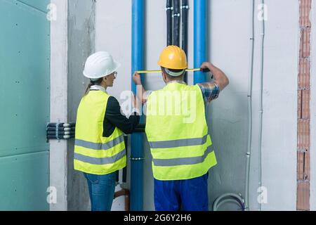 Construction workers measuring pipes on site with tape Stock Photo