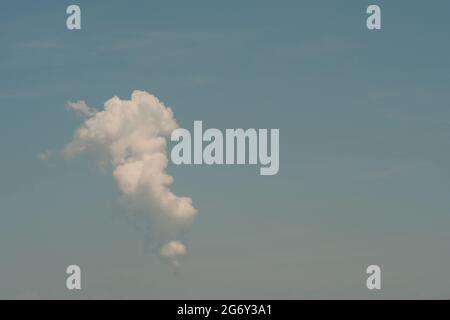 Single puffy whiote cloud in hazy blue summer sky with negative space for copy Stock Photo
