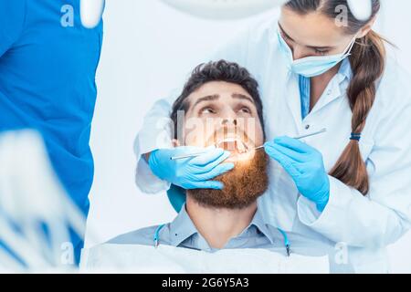 Side view of a reliable female dentist, using sterile instruments and blue surgical gloves while cleaning the teeth of a patient in the dental office Stock Photo