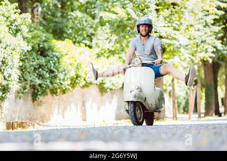 Happy carefree young man driving retro scooter Stock Photo