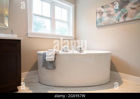 A large luxury ceramic bath tub in a home bathroom with towels Stock Photo