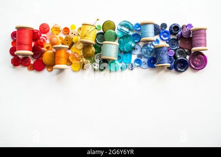 A lot of buttons and reels with colorful threads, laid out on a white background in the colors of the rainbow. Copy space. Stock Photo