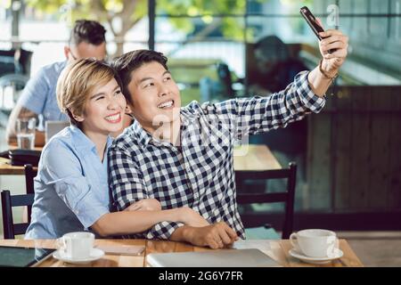Portrait of young couple taking selfie in the cafe through cellphone Stock Photo