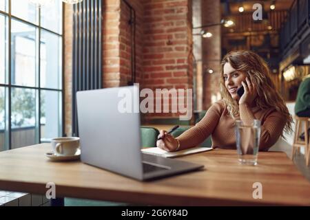 Pretty woman taking notes while talking on mobile Stock Photo