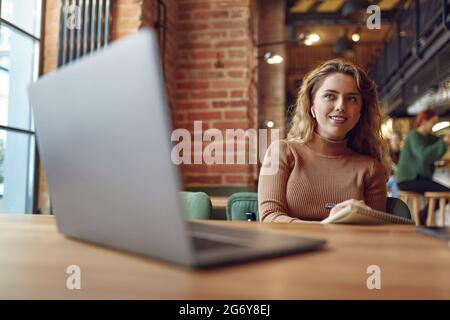 Woman using earphones and laptop for studying at cafe Stock Photo