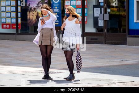 Dundee, Tayside, Scotland, UK. July, 2021. UK Weather: Humid day with a warm breeze and sunny intervals across North East Scotland with temperatures reaching 18°C. Two fashionable women together outside wearing facemasks holding their I Phones whilst enjoying the warm sunshine in Dundee city centre. Credit: Dundee Photographics/Alamy Live News