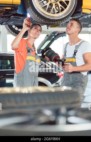 Experienced female auto mechanic checking tires before installing together with her colleague a new air suspension system in a modern automobile repai Stock Photo