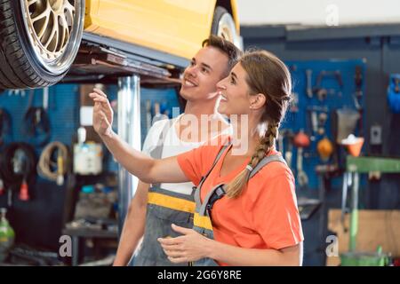 Two happy dedicated auto mechanics, checking the modified wheels of a tuned car while working together in a modern automobile repair shop with tuning Stock Photo
