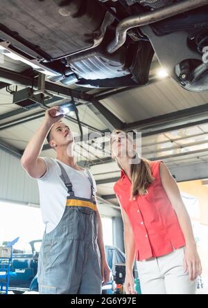 Low-angle view of a reliable auto mechanic holding a flashlight, while checking the parts of the lifted car of a woman in a modern automobile repair s Stock Photo