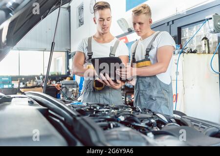Experienced auto mechanic using a laptop for scanning and interpreting engine error codes next to an apprentice in a modern automobile repair shop Stock Photo
