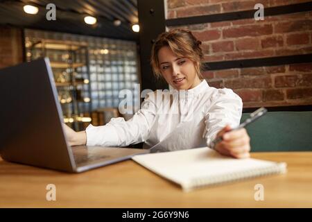 Pleasant woman taking notes while working on laptop Stock Photo