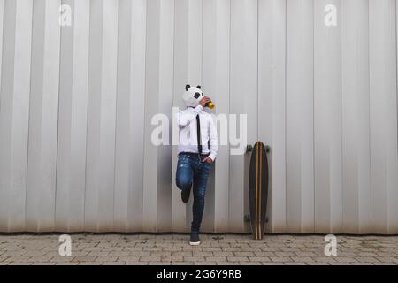 Businessman with a longboard skateboard and panda bear mask having coffee Stock Photo