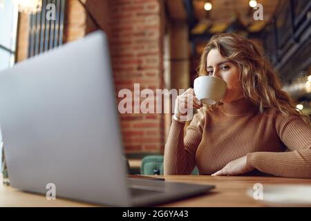 Female freelancer working on laptop and drinking coffee Stock Photo
