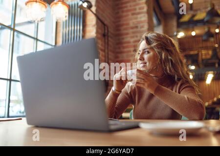 Woman drinking coffee and working on laptop at cafe Stock Photo