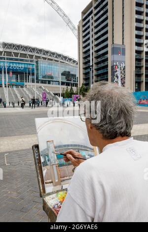 Wembley Stadium, Wembley Park, UK. 9th July 2021.   Wembley Park is buzzing with excitement ahead of Sundays match.  London based artist, Nick Botting, previously commissioned to paint the FA Cup Final, sits on Olympic Way, painting Wembley Stadium to create an artwork of this historic occasion.   60,000 fans are set to descend to Wembley Park to watch England play Italy in the UEFA EURO 2020 Finals at Wembley Stadium on Sunday 11th July.  Amanda Rose/Alamy Live News Stock Photo
