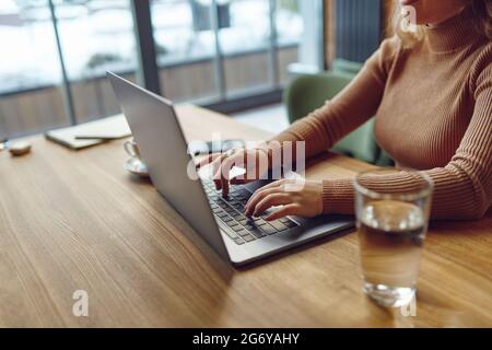 Woman typing on laptop while working remotely from cafe Stock Photo