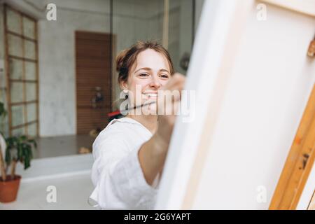 Happy woman painting on easel with brush Stock Photo