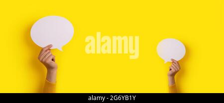 hands holding dialogue icon over yellow background, panoramic mock-up image Stock Photo