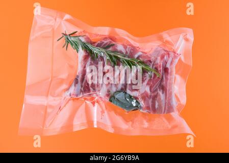 spare pork ribs with rosemary in vacuum packed sealed for sous vide cooking, isolated on orange background Stock Photo