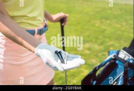 Close-up of the hand of a woman wearing white glove, while holding three tees in the beginning of the game outdoors on a professional golf course Stock Photo