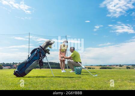 Full length of an experienced male instructor teaching a young woman the correct grip of the golf club on a green field in summer Stock Photo