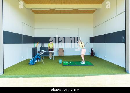 Full length view of a dedicated golf coach using modern equipment, while teaching a young woman the correct movement for striking the ball as a profes Stock Photo