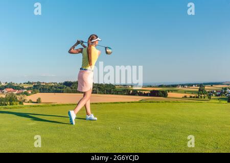 Full length of a professional female golf player smiling while swinging a driver club with concentration and accuracy before hitting the ball during i Stock Photo