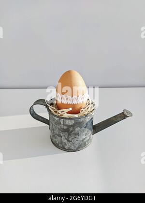 Easter egg in small decorative steel watering can on light background. Easter DIY table decoration Stock Photo