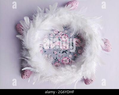 White feathers wreath on lilac floral background with decorative easter eggs, top view. DIY Easter decoration at home concept Stock Photo