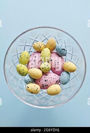 Colored decorative easter eggs in crystal vase on blue background, top view. DIY Easter decoration at home Stock Photo
