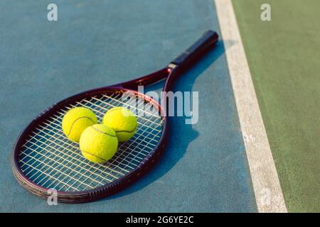 High-angle close-up of three fluorescent yellow tennis balls on a professional racket on the acrylic blue surface of a modern tennis court Stock Photo