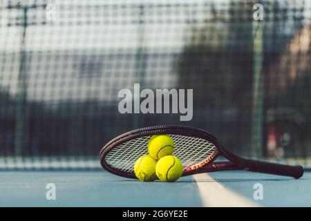 High-angle close-up of three fluorescent yellow tennis balls on a professional racket on the acrylic blue surface of a modern tennis court Stock Photo