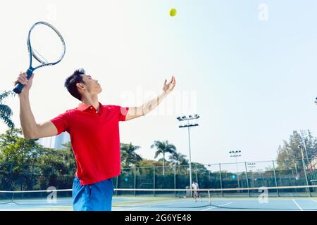 Chinese professional tennis player ready to hit the ball with the racket after tossing while serving in the beginning of a difficult match Stock Photo