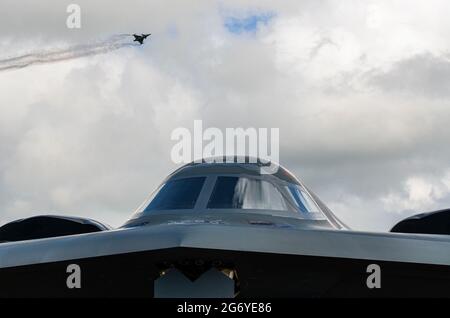 Northrop Grumman B-2 Spirit stealth bomber with flying jet fighter at RAF Fairford Royal International Air Tattoo airshow. Menacing shaped aircraft Stock Photo