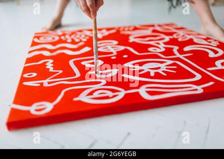 Close up of woman painting abstract drawing on red canvas Stock Photo