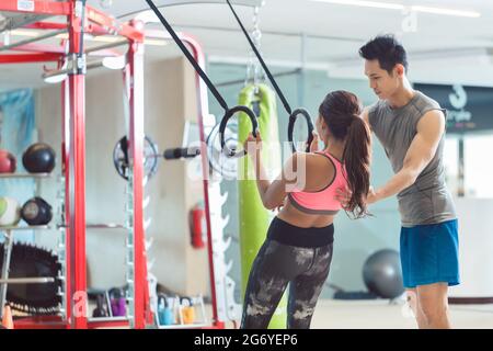 Low-angle view of a beautiful young woman smiling while doing push-ups on gymnastic rings during workout at the gym Stock Photo