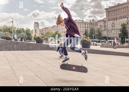 A teenage boy rides a skateboard on the square. Performing stunts, extreme sports. Stock Photo