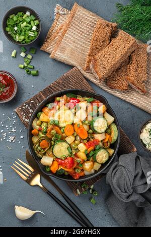 Baked vegetables in a frying pan on a gray background with herbs and bread. Stock Photo