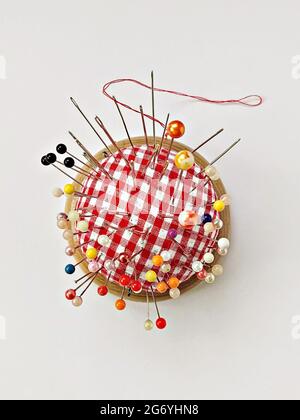 Round pin cushion with lot of pins, yellow thimble, spool of thread and scissors. Sewing accessories flat lay on white background Stock Photo