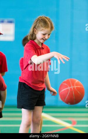 Primary school girl child / kid takes part in basketball dribbling ball bouncing on school sports day  at the end of the academic year & schools term Stock Photo