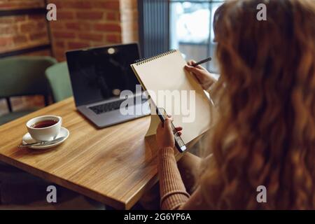 Woman using smartphone and writing in notebook Stock Photo