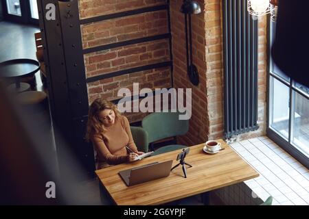 Woman taking notes while working on laptop Stock Photo