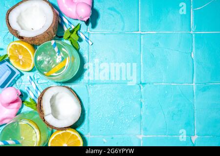 Bright sunny summer vacation. Lemonade drink on wet blue pool tiles background, with beach holiday accessories, flamingo lifebuoys, lemons, coconuts, Stock Photo