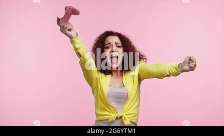 KYIV, UKRAINE - JUNE 30, 2021: amazed young woman holding gamepad and rejoicing isolated on pink Stock Photo